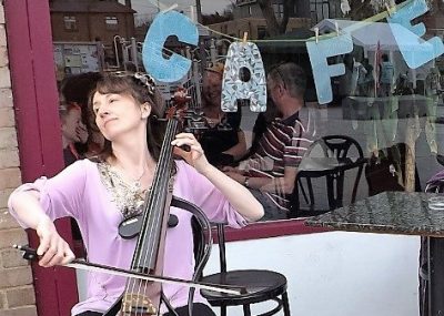 Joanne plays cello soulfully in front of a cafe window