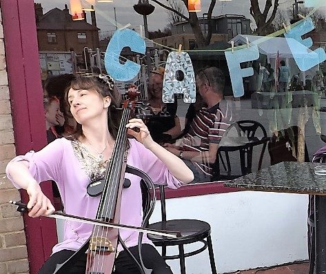 Joanne plays cello soulfully in front of a cafe window