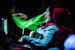 A young girl in a wheelchair smiles as a colourful scarf drifts past her face
